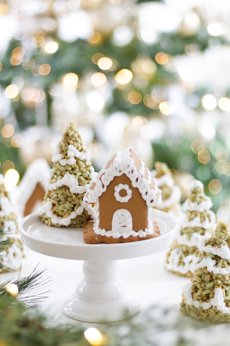 A decorated tree and a decorated gingerbread house on the cake stand together.