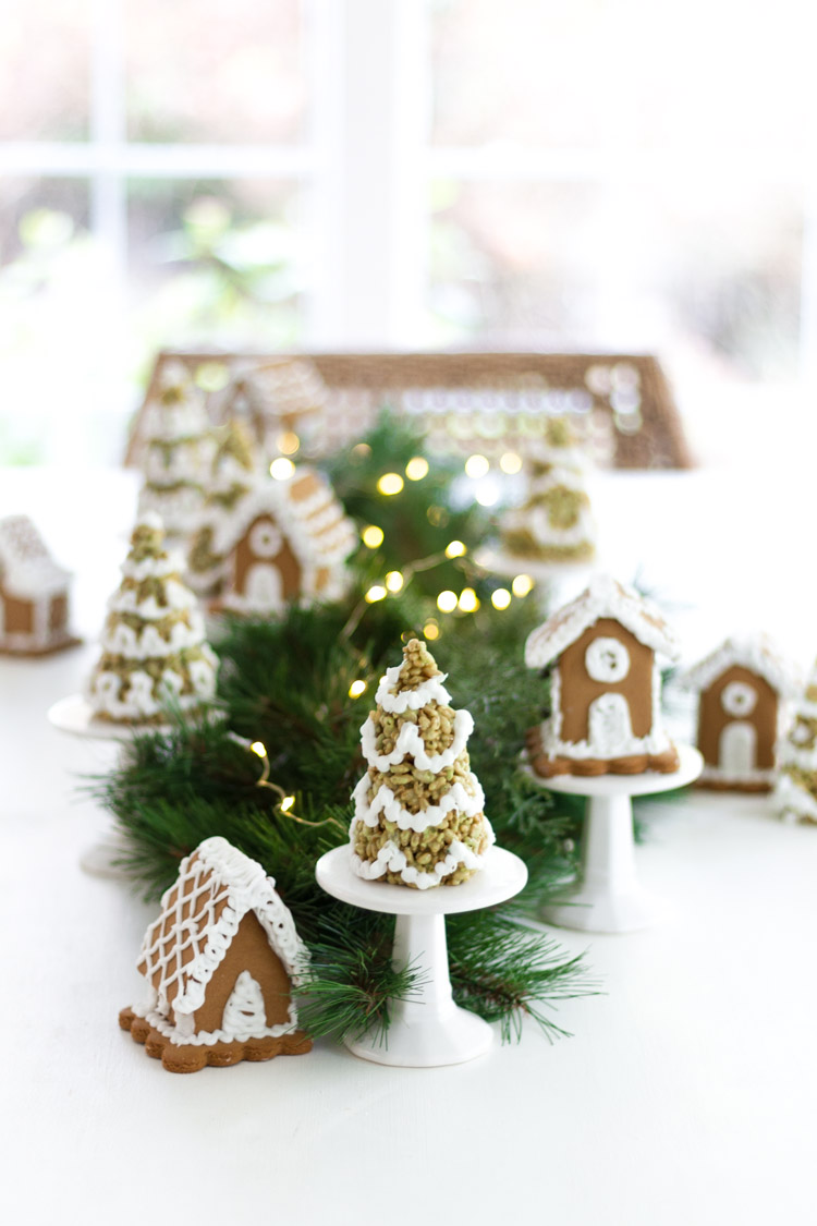 Little gingerbread houses and little Christmas trees on stands beside them on the table.