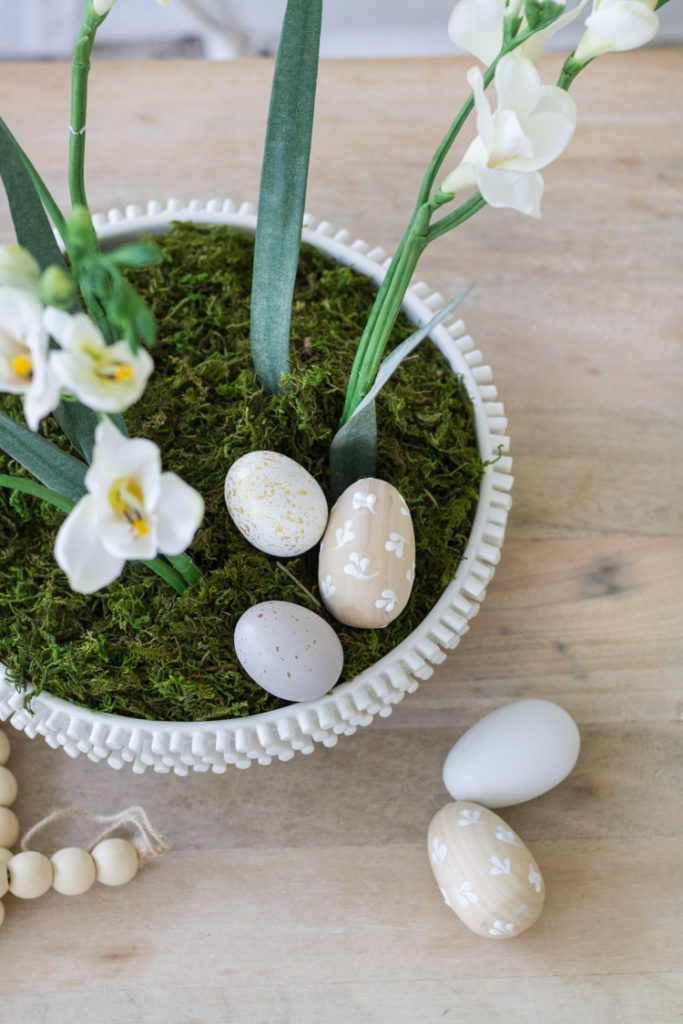 A planter with white daffodils and green moss with the eggs scattered around it.