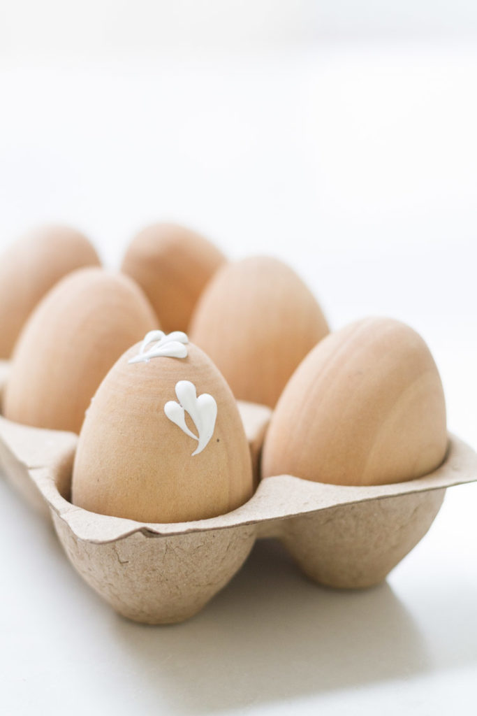 The eggs in a egg crate being painted with white flowers.