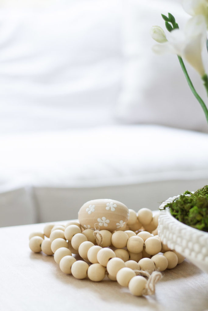 Wooden beads and a wooden egg that has little painted white flowers on it on the table.